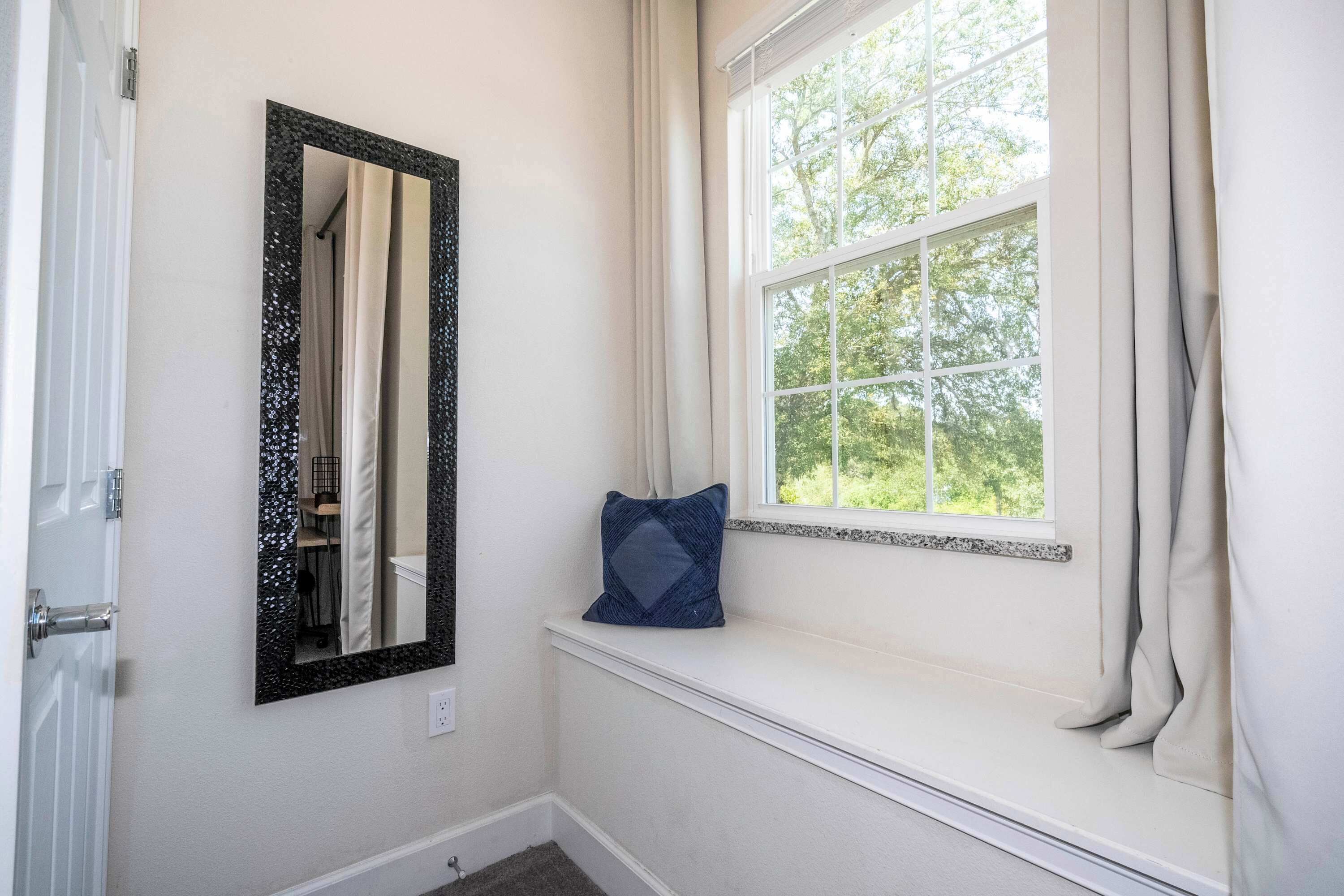 A bathroom with a window, a mirror, and a blue pillow on a ledge.