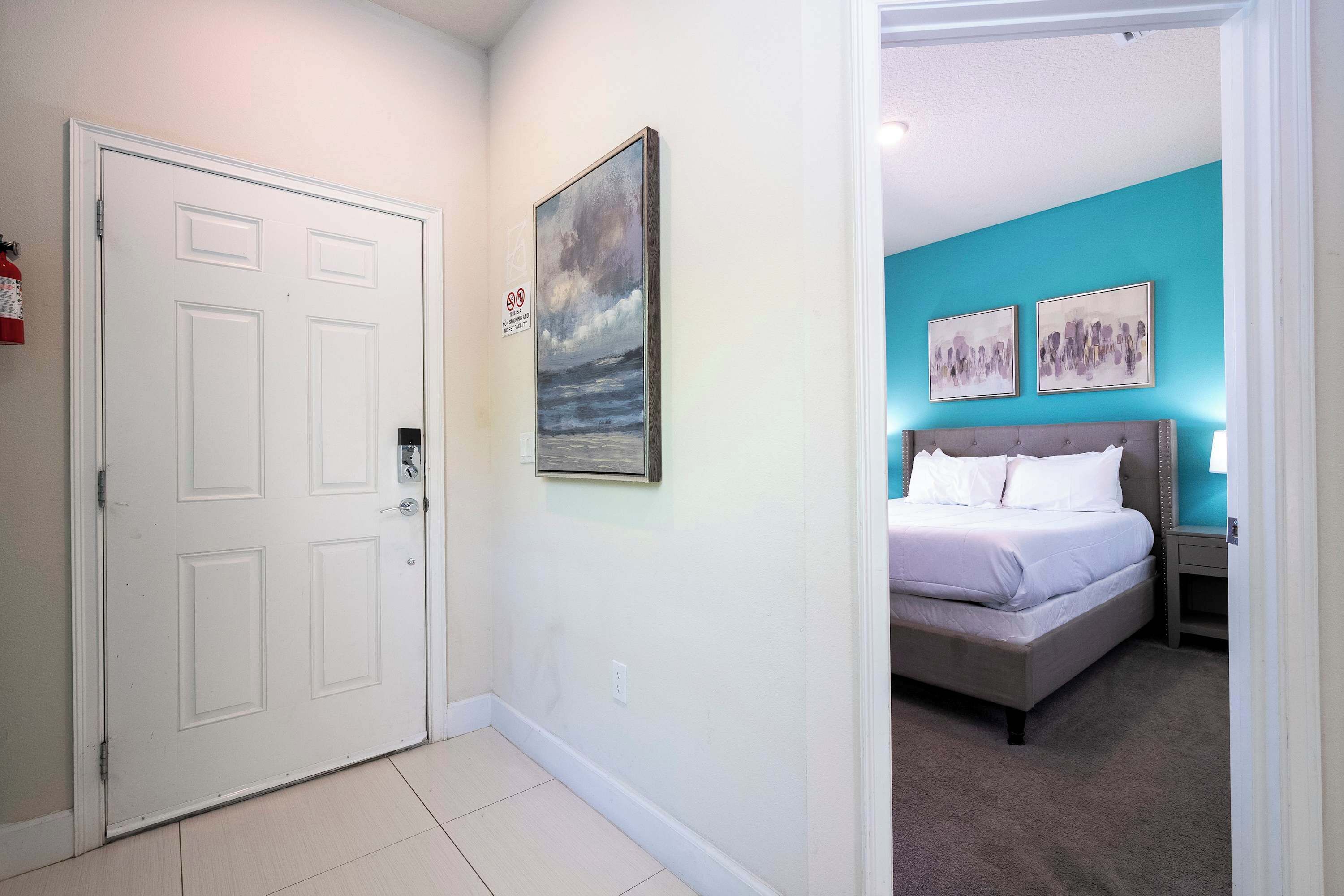 A hotel room with a bed, a nightstand, a painting on the wall, and a white door.