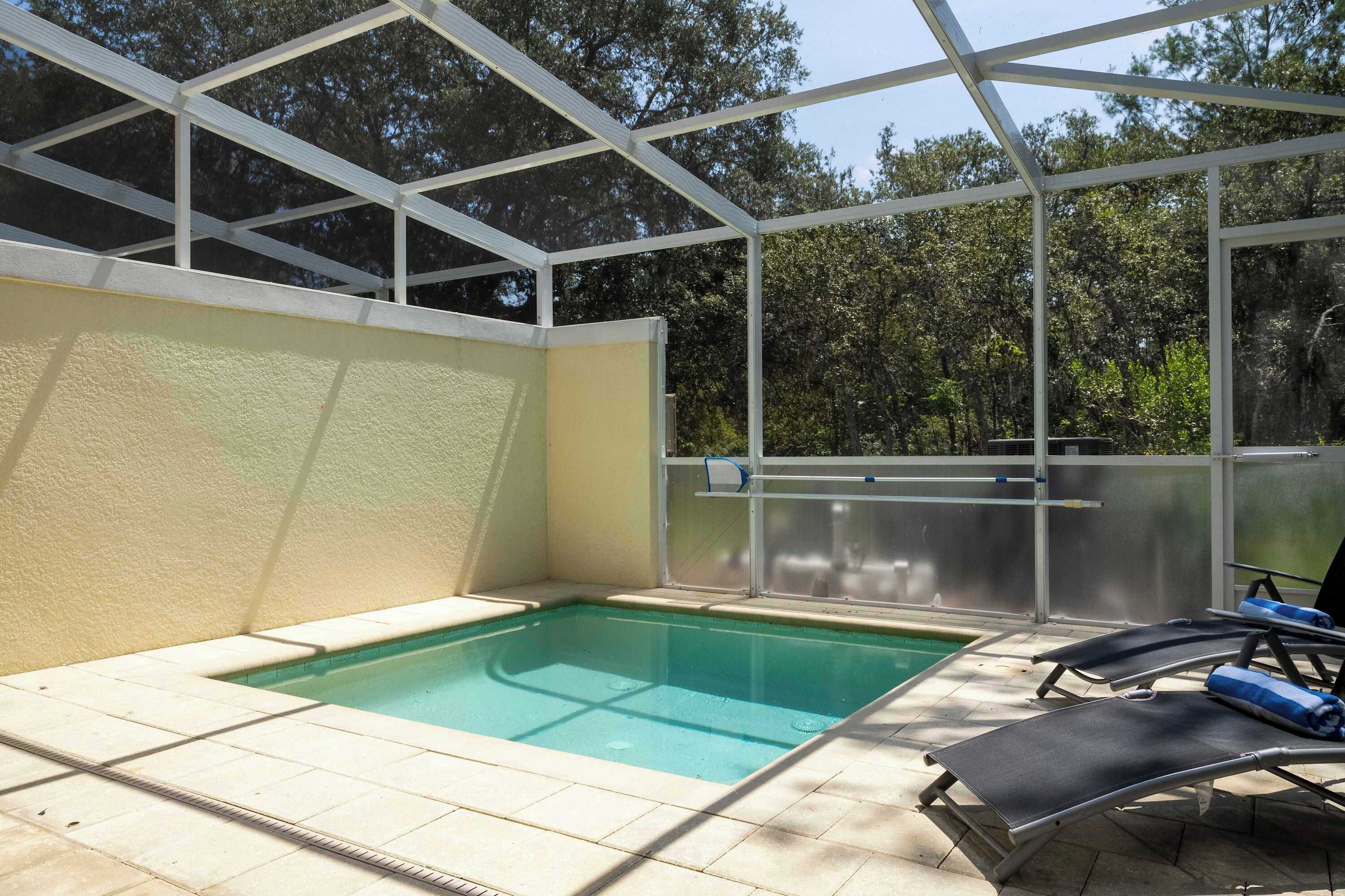 A swimming pool with a glass enclosure, surrounded by lounge chairs and a view of trees.