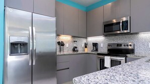 Une cuisine moderne dotée d’appareils électroménagers en acier inoxydable, de plans de travail en granit et d’un mur d’accent bleu.