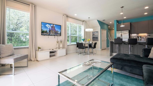 Un salon moderne avec une table basse en verre, un canapé, un téléviseur et un coin repas comprenant des chaises et une table.