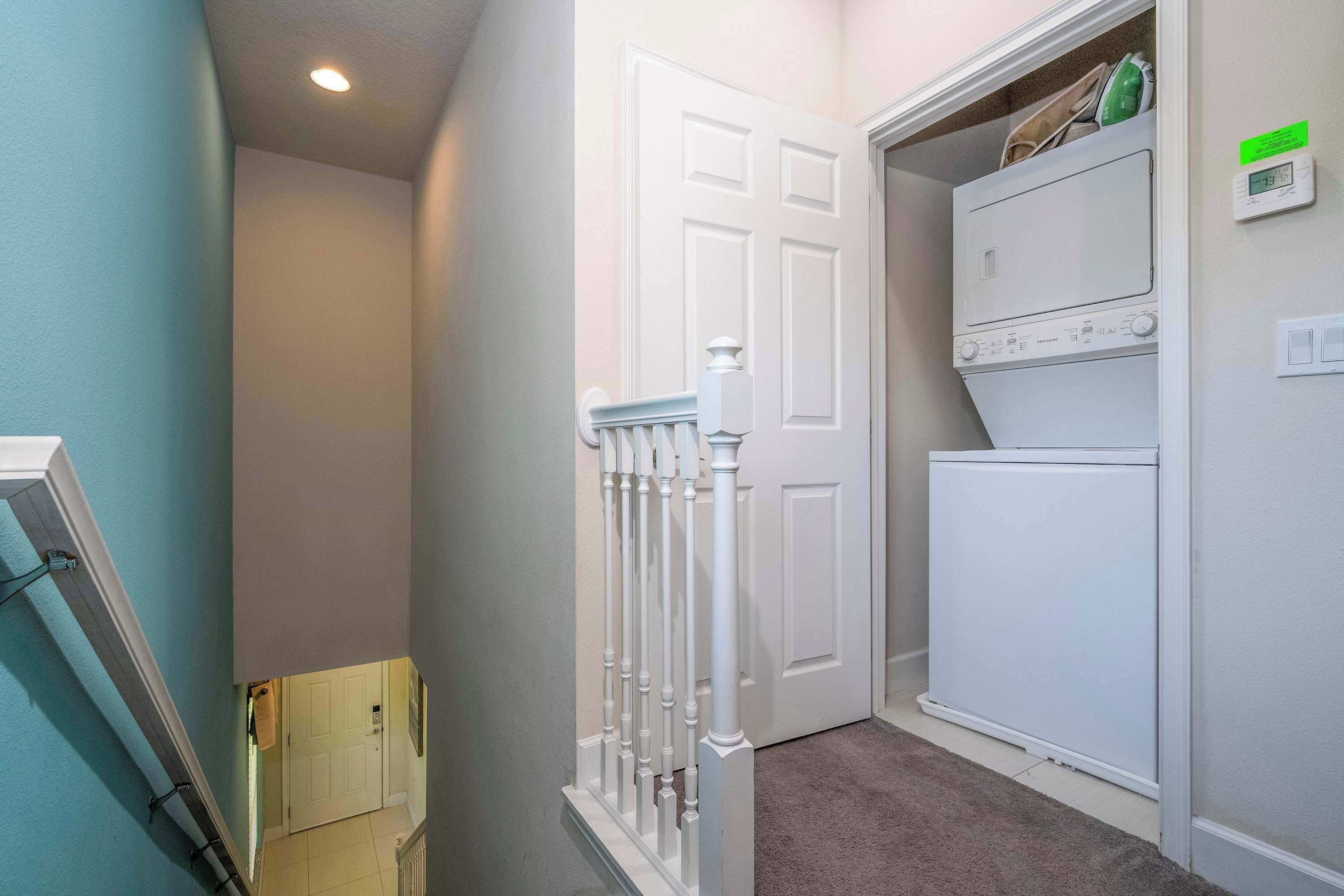 A laundry room with stacked dryers and a thermostat on the wall.