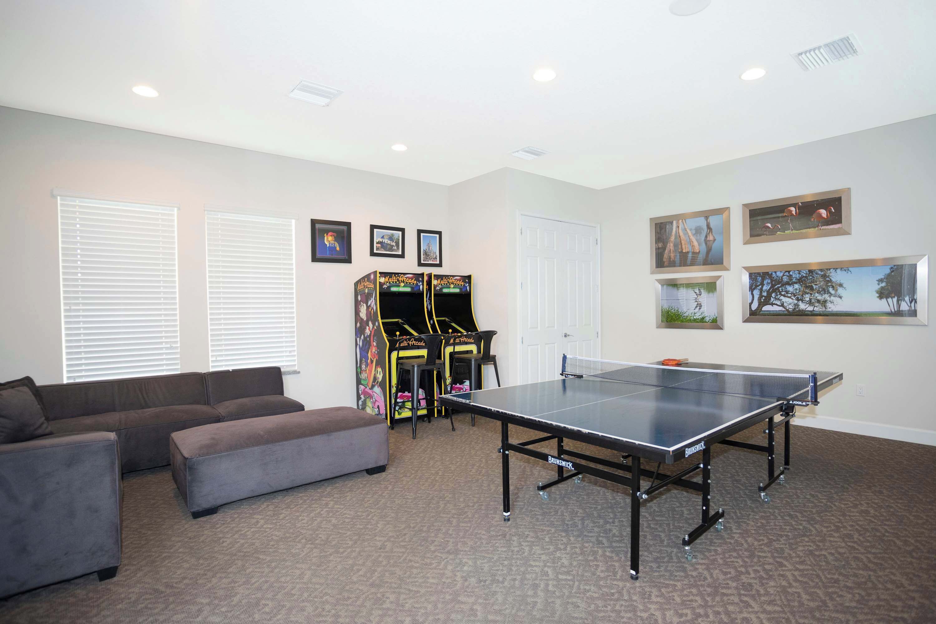 Ein Zimmer mit Tischtennisplatte, grauem Sofa und Spielautomaten.