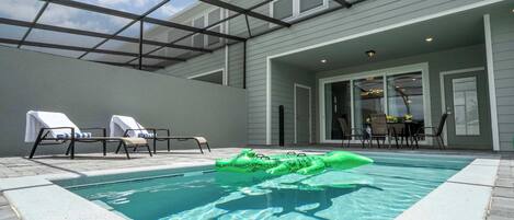 A swimming pool with a green inflatable crocodile toy, lounge chairs, and a covered patio area.