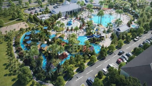 Luchtbeeld van een resort met meerdere zwembaden, weelderige begroeiing en een parkeerplaats.