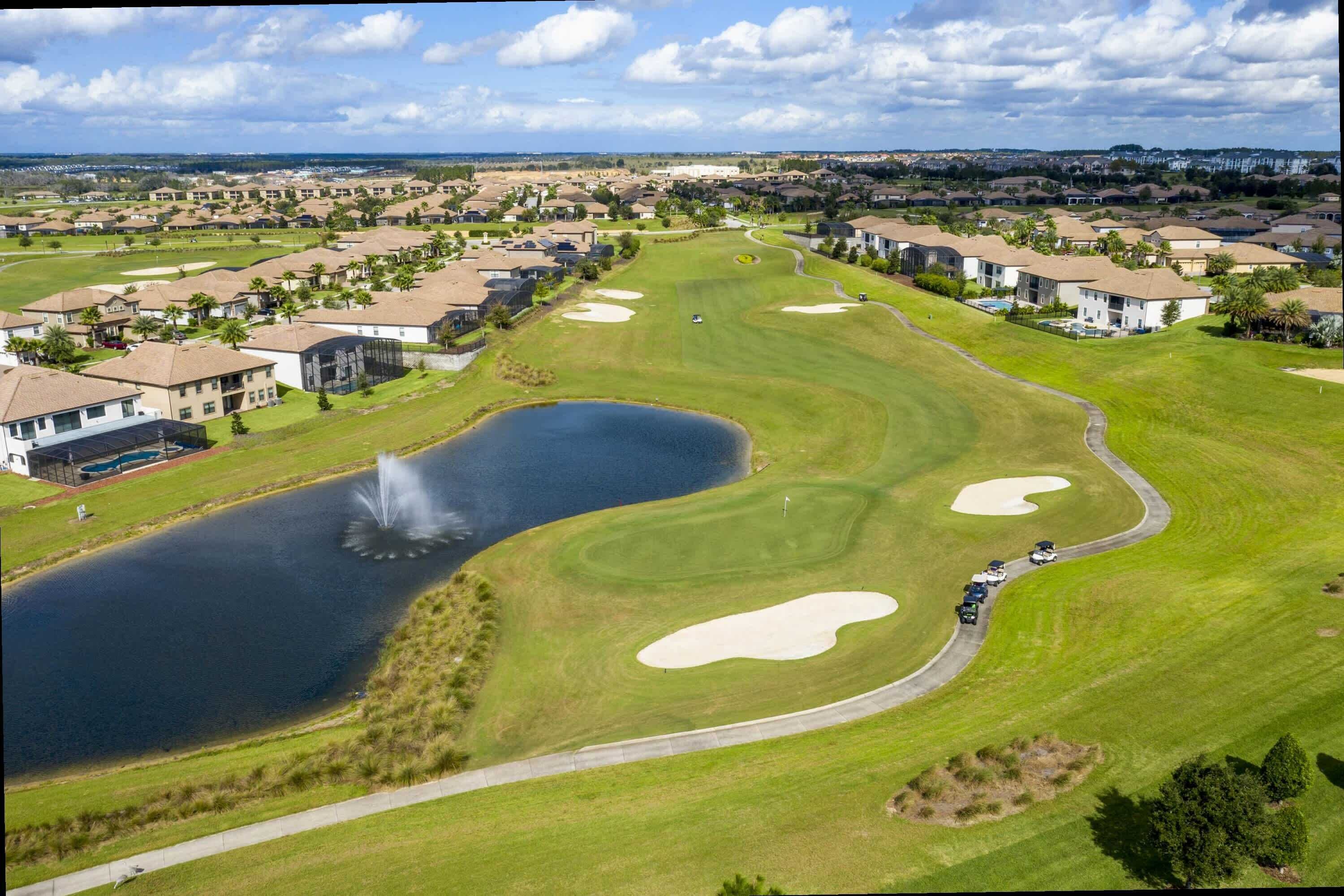 A golf course with bunkers, a pond, and residential buildings in the background.