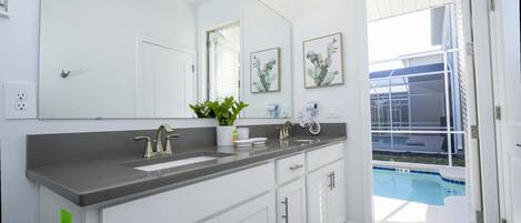 A modern bathroom with a large mirror, white cabinets, a grey countertop, and a view of a swimming pool.