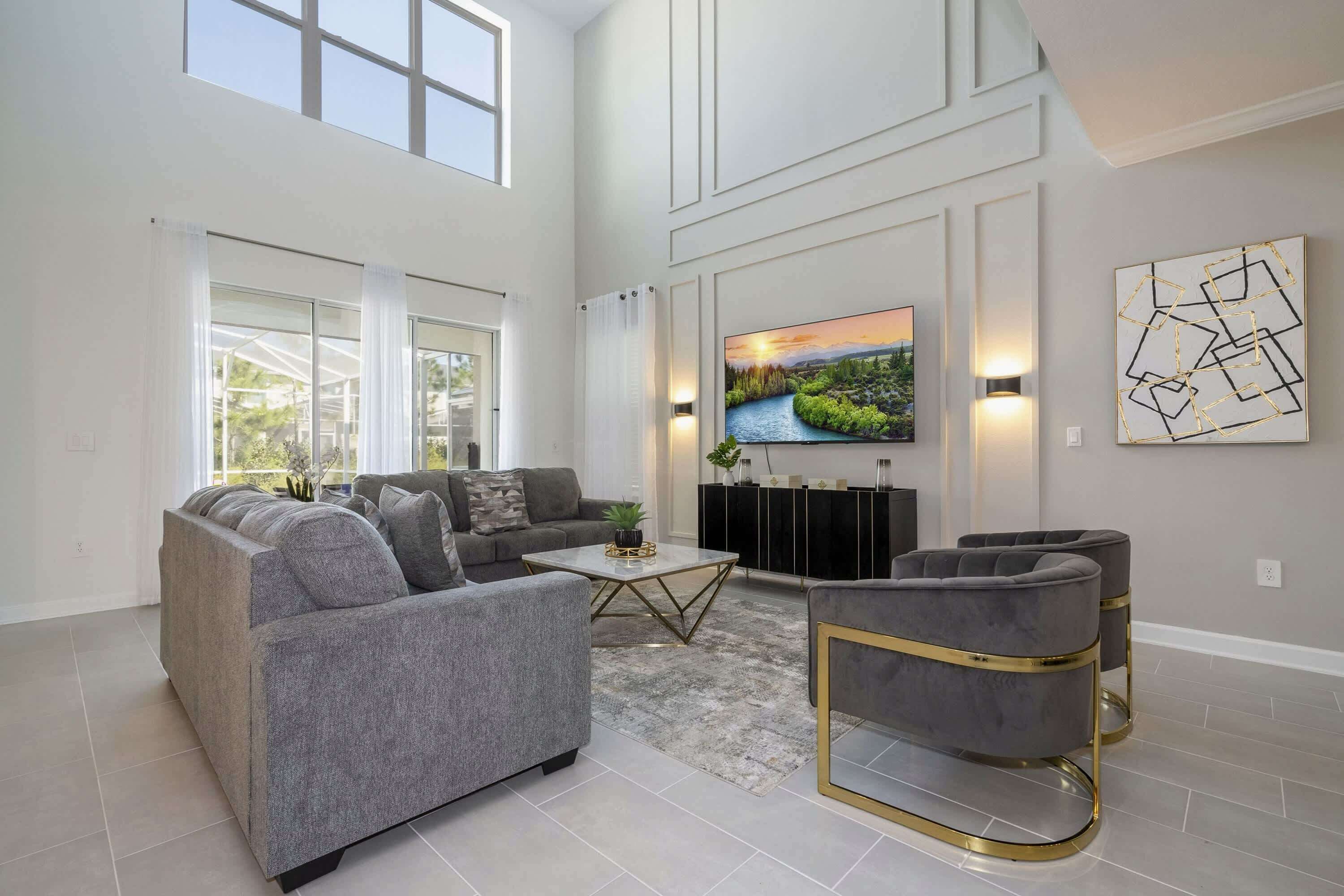 A spacious living room with a grey sofa set, a coffee table, and a TV mounted on the wall.