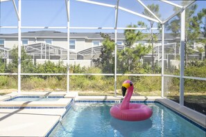 Uima-allas, jossa on vaaleanpunainen flamingo-uimapatja, ja jonka ympärillä on lasiseinä, josta avautuu näkymä asuinalueelle.