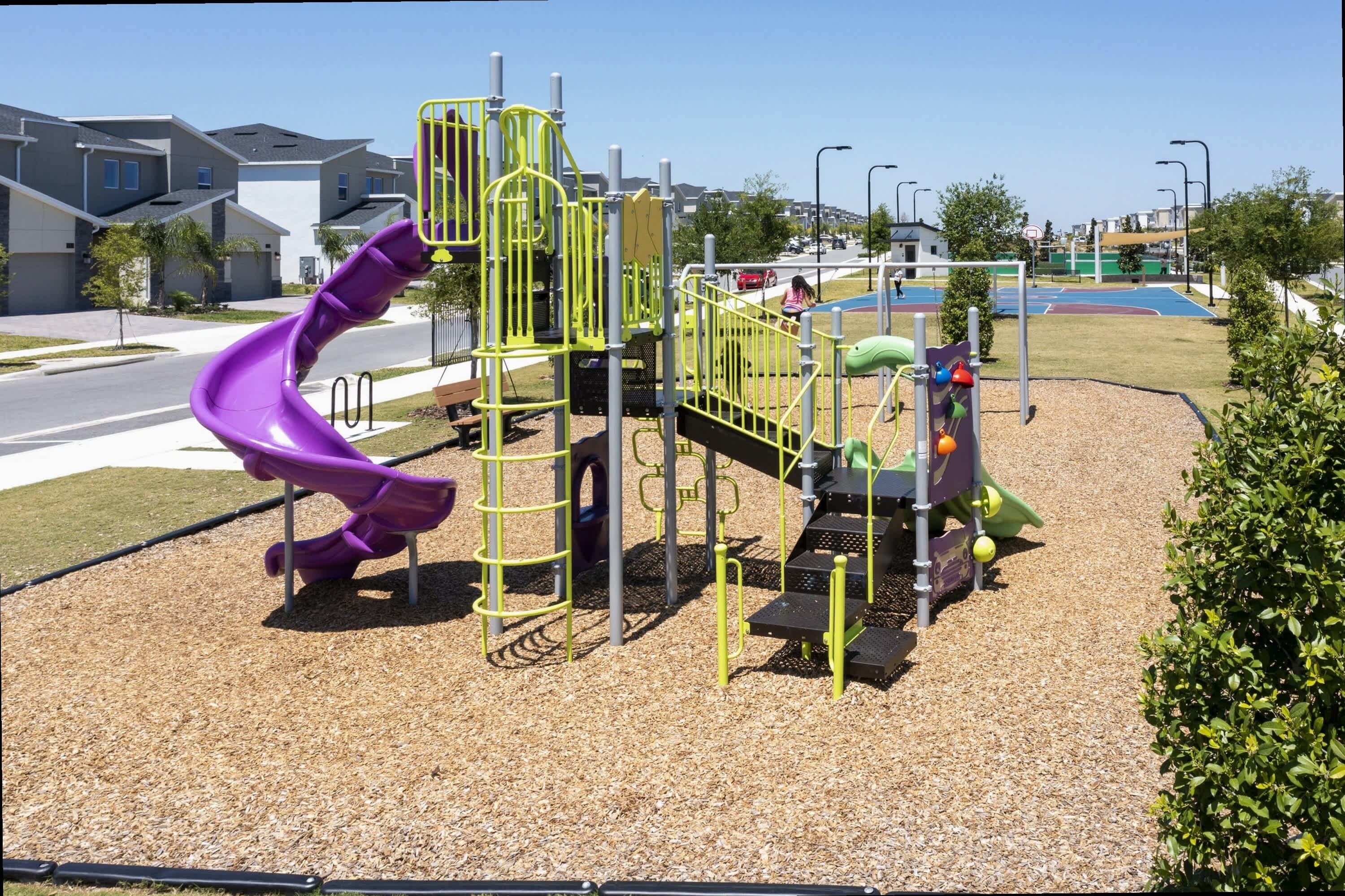 A playground with a purple slide and climbing structures, surrounded by a residential area.