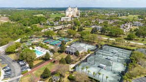 Luchtbeeld van een resort met een groot gebouw, meerdere tennisbanen, een zwembad en veel groen eromheen.