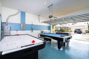 An indoor recreational area with two foosball tables and a pool table, a water heater, and a bicycle in the background.