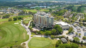 Een groot hotel met meerdere verdiepingen, omgeven door goed onderhouden golfbanen en parkeerplaatsen.