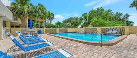 A swimming pool area with blue lounge chairs and a poolside table.