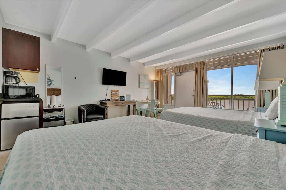 A hotel room with two beds, a desk, a chair, a television, and a balcony with a view.