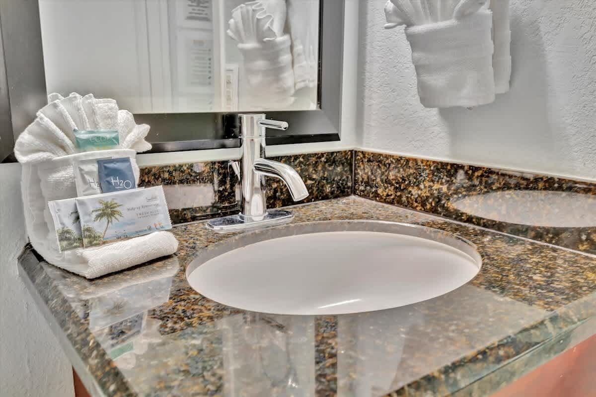 A bathroom with a granite countertop, a white sink, and a mirror above it. There are towels hanging on the wall and a tissue box on the counter.