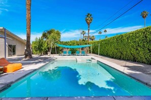 A swimming pool with lounge chairs and a canopy, surrounded by palm trees and a hedge. - Modern Paradise at Sonora (Palm Desert)
