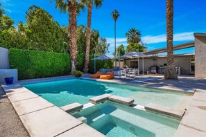Ein Pool mit Whirlpool, umgeben von Palmen und einer Terrasse mit Gartenmöbeln.