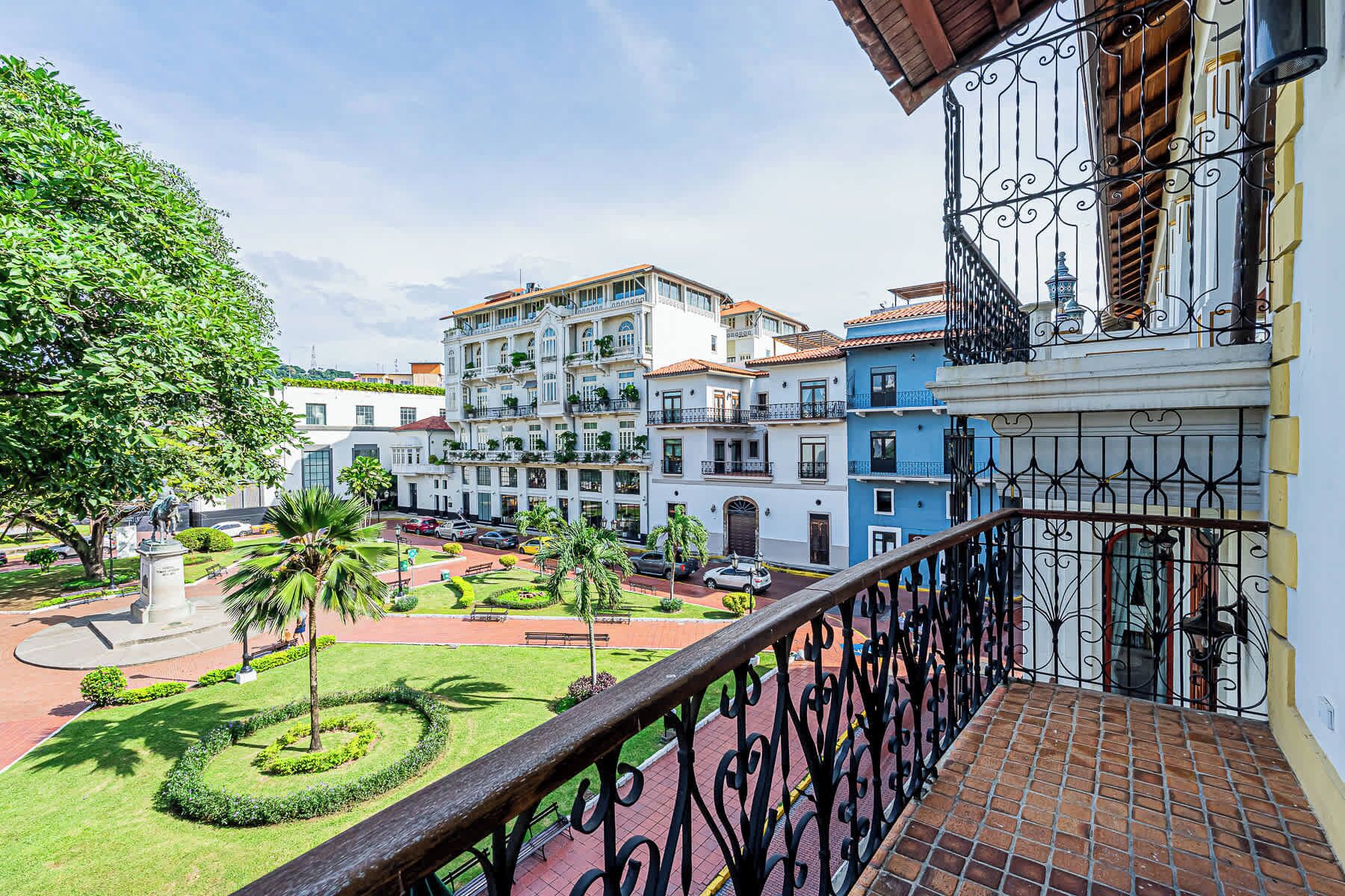 A balcony with wrought iron railings overlooking a courtyard with neatly trimmed grass, a statue, and a fountain.