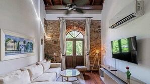 A living room with a stone wall, a sofa, a TV, and a ceiling fan. - w Grandiose 1BR w Balcony in San Felipe (Panama City)