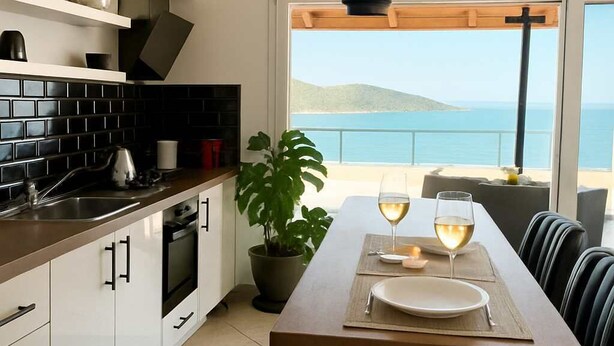 A modern kitchen with a dining area overlooking a scenic view. - Panoramic Seaview Blue Nest - Stylish Getaway (Amfilochia)