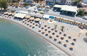 Un hotel frente a la playa con tumbonas, sombrillas y una carretera al fondo.