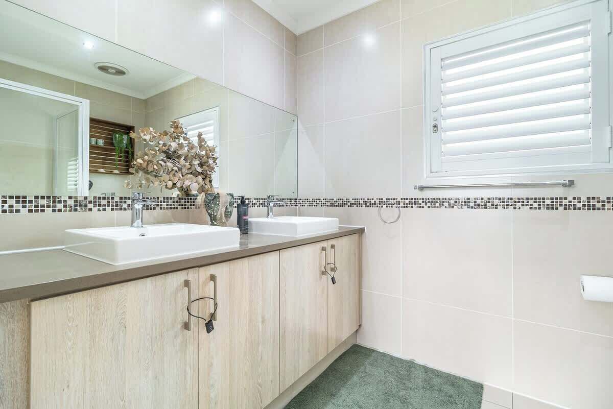 A modern bathroom with two sinks, a large mirror, and a window with blinds.
