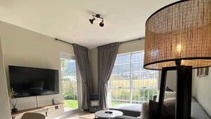 A modern living room with a flat-screen TV, a sofa, a coffee table, and a lamp. - 2 Bedroom Ground Floor Apartment Princess Beach Club Houtbay (Cape Town)