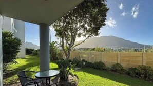 A patio with a table and chairs, a small tree, and a view of a mountain. - 2 Bedroom Ground Floor Apartment Princess Beach Club Houtbay (Cape Town)