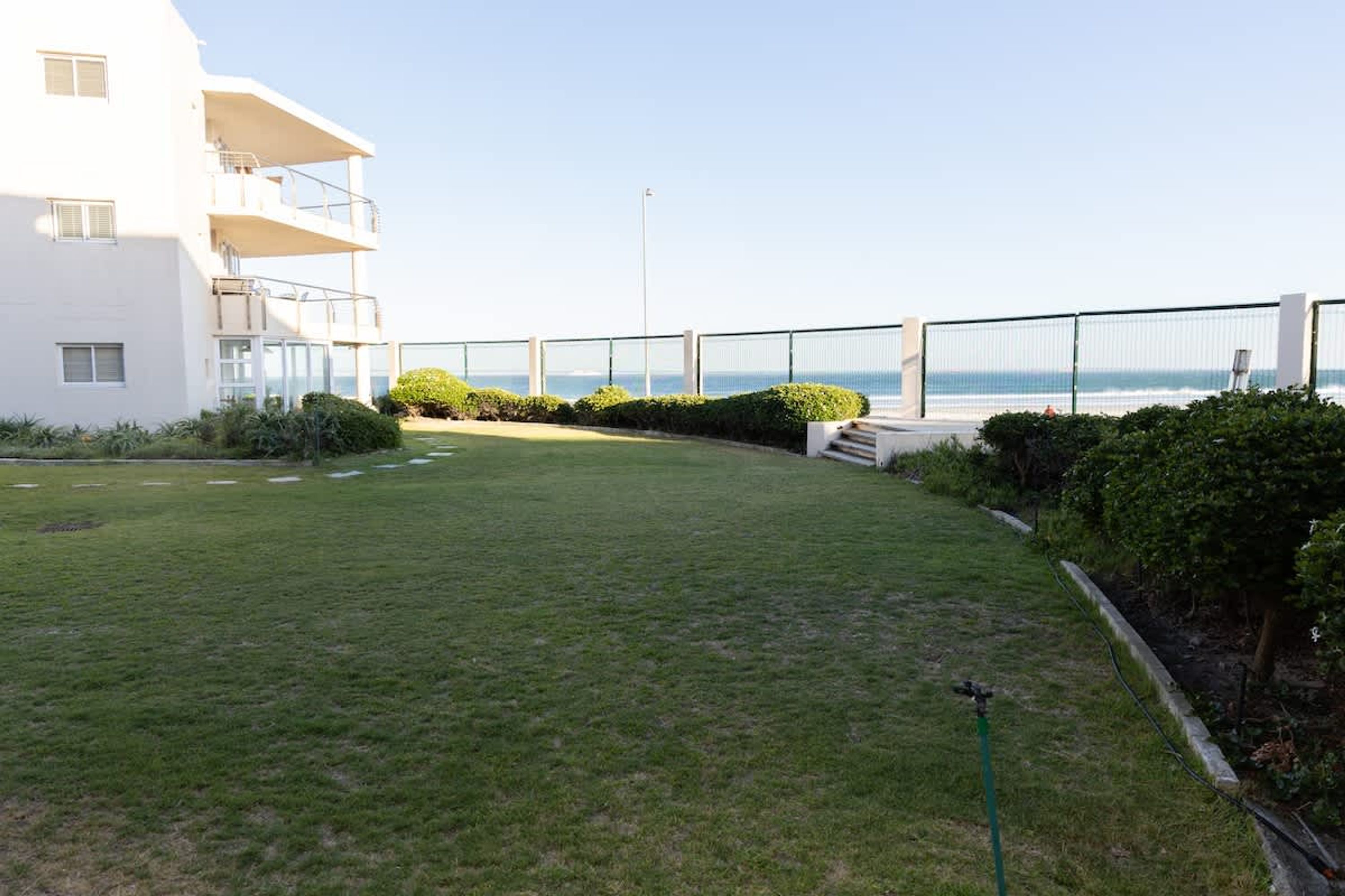 A white building with a balcony, a grassy yard, and a view of the sea.