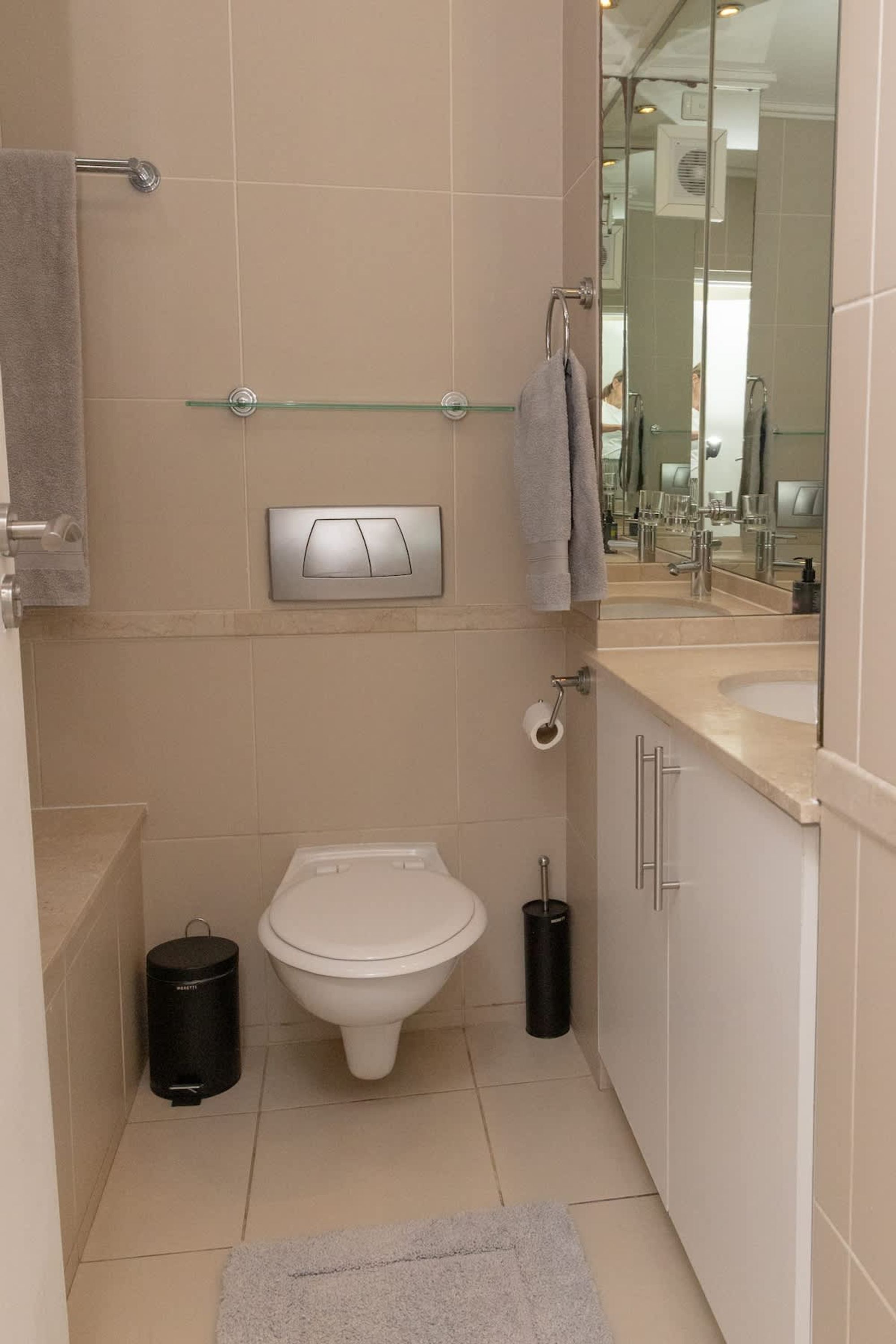 A modern bathroom with a toilet, bidet, glass shelf, and a mirror.