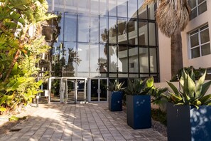 Un bâtiment moderne doté d’une façade en verre, d’une entrée avec une porte en verre et de plantes en pot.