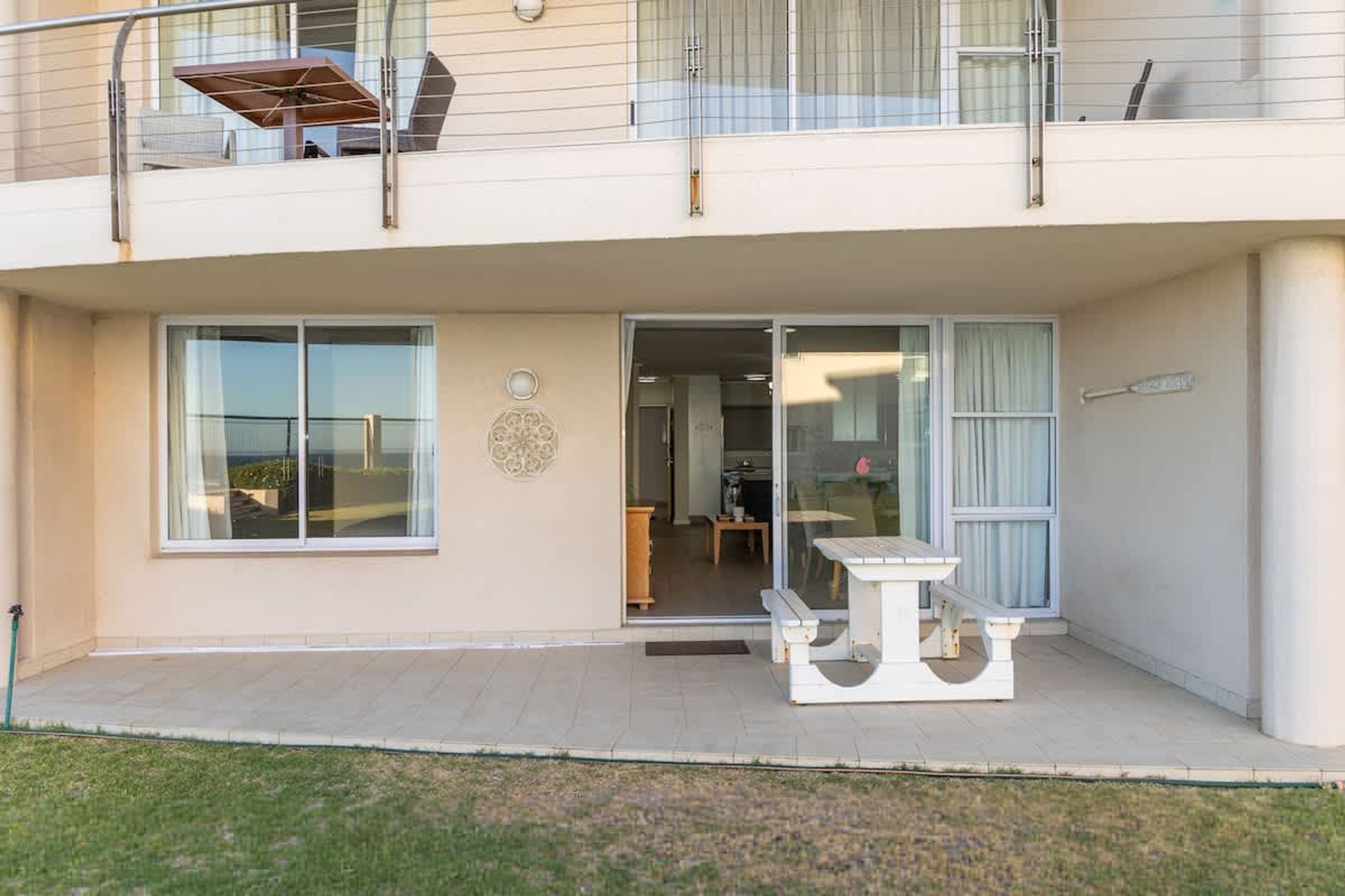 Un edificio de dos pisos con un balcón, un patio con mesa y sillas, y ventanas amplias.