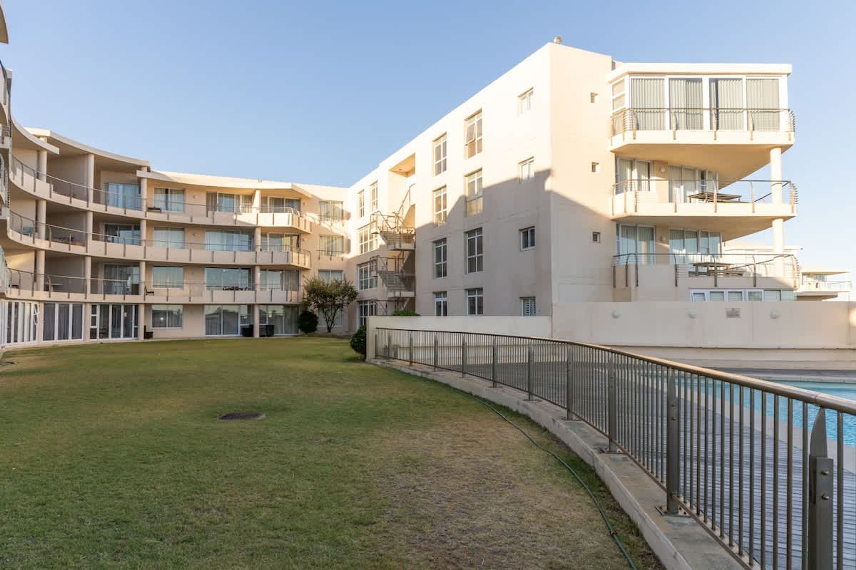 Un edificio residencial de varios pisos con balcones, una piscina y un patio césped.