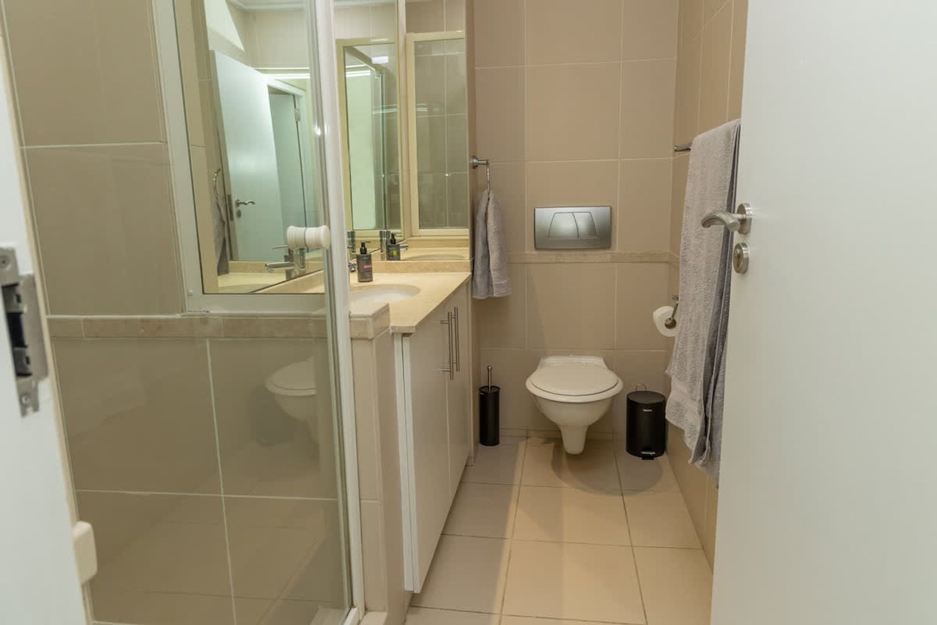 A modern bathroom with a glass shower enclosure, a toilet, a sink with a mirror, and a towel rack.