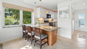 A modern kitchen with a central island, white cabinetry, and pendant lighting. - Olde Naples Condo – Walk to Beach & Dining (Naples)