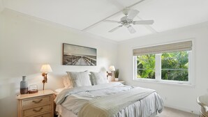 A bedroom with a bed, bedside lamps, a nightstand, a ceiling fan, a window with blinds, and a painting on the wall. - Olde Naples Condo – Walk to Beach & Dining (Naples)