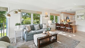 A spacious living room with a grey sofa, a coffee table, and a dining area with wooden chairs. - Olde Naples Condo – Walk to Beach & Dining (Naples)