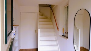 Una escalera con peldaños blancos y barandilla de madera que lleva a una puerta con picaporte de latón.