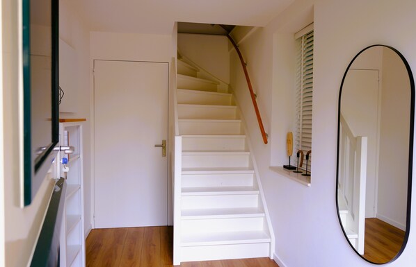 Una escalera con peldaños blancos y barandilla de madera que lleva a una puerta con picaporte de latón.