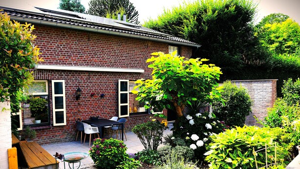 Una casa de ladrillo con un patio, mobiliario exterior y un jardín con diversas plantas y flores.