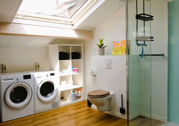 Un baño moderno y compacto con tragaluz, lavadora, inodoro y cabina de ducha de vidrio.