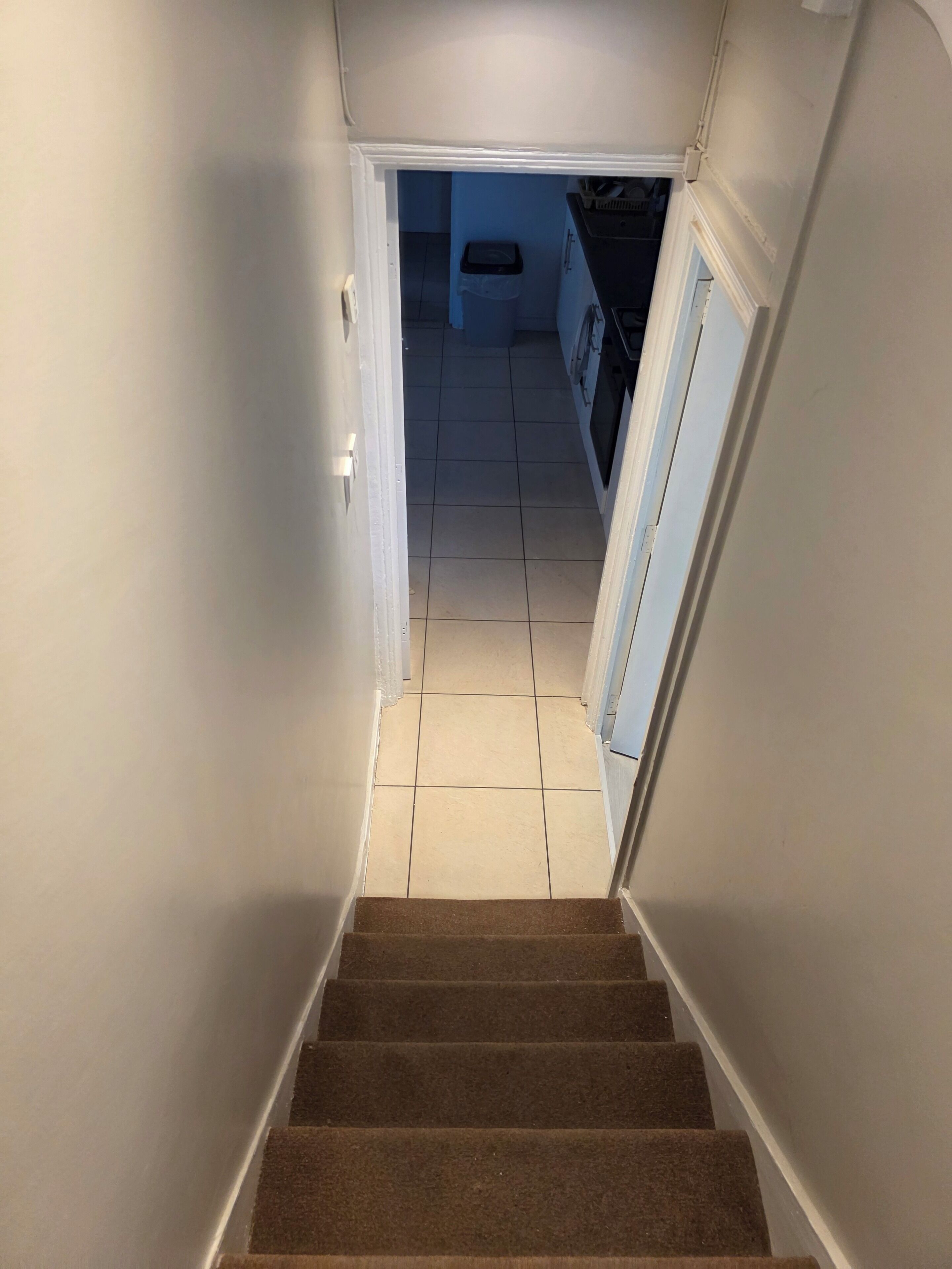 A staircase leading to a kitchen with white walls and a tiled floor.