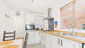 A modern kitchen with white cabinets, stainless steel appliances, a wooden countertop, and a window with blinds.