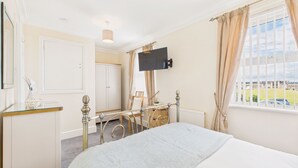 A bedroom with a bed, a TV mounted on the wall, a window with curtains, a radiator, and a wardrobe.
