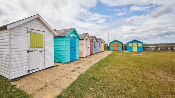 A row of colorful beach huts with a grassy area in front.