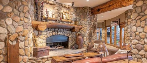 A stone-walled room with a fireplace, leather seating, and a wooden table.