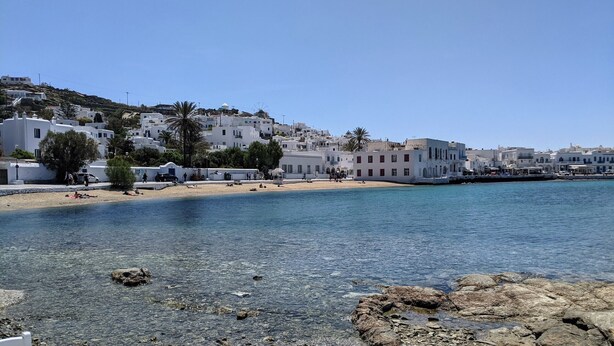 A coastal town with white buildings, clear blue water, and rocky shoreline.