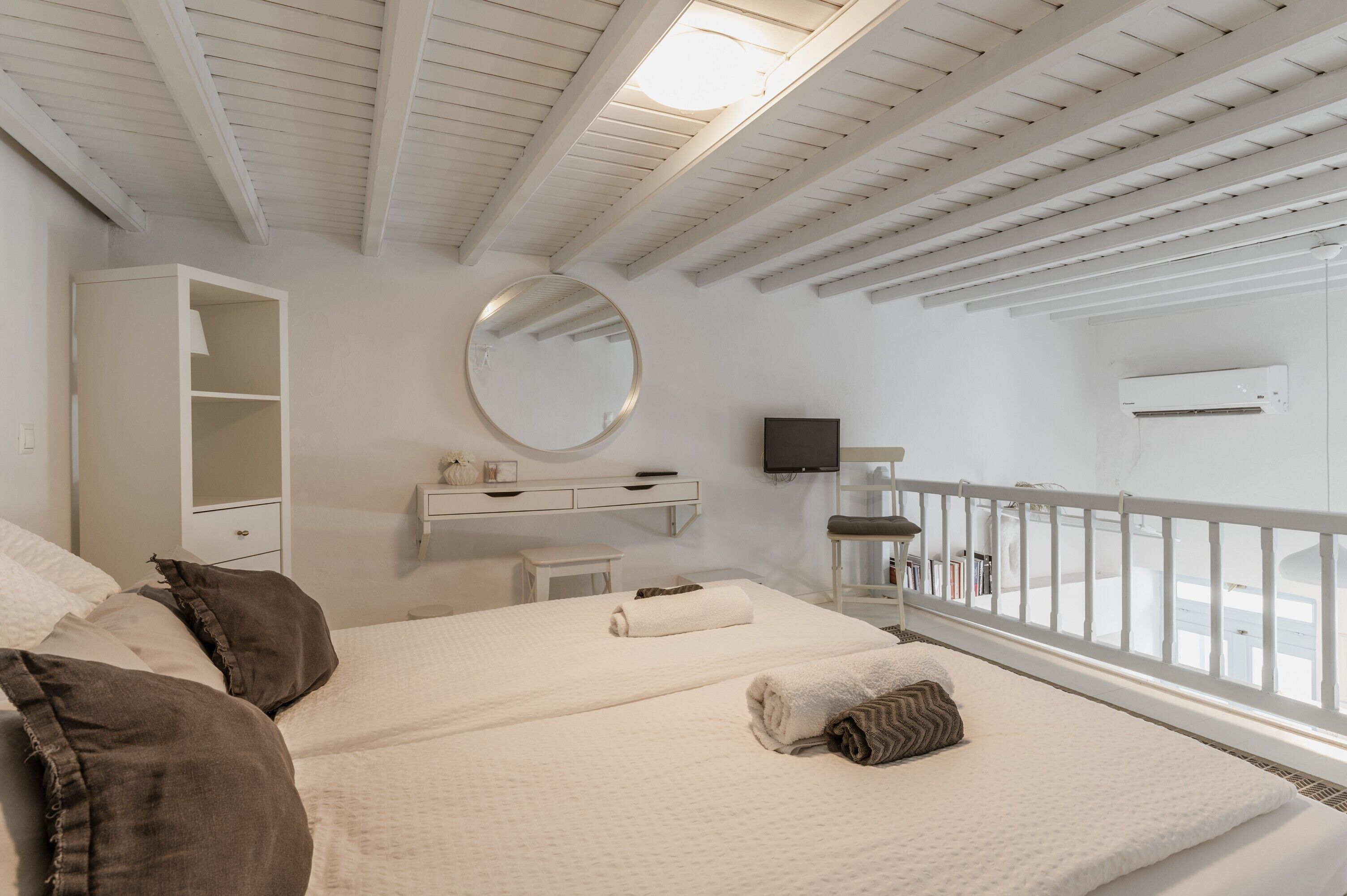 Une chambre à coucher comprenant un lit, une armoire, un miroir, une télévision et un balcon avec une balustrade.