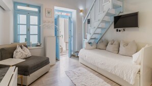 A room with a sofa, a bed, a TV, a staircase, and a door.